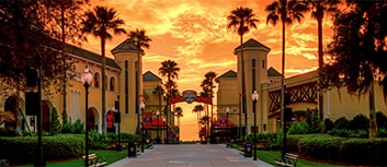 A palm tree and lamppost-lined concrete path leads to an archway with the ESPN Wide World of Sports Complex logo at sunset